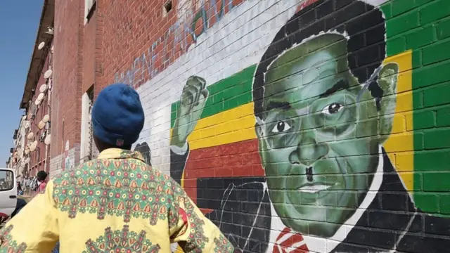 A man stands next to a mural of Robert Mugabe
