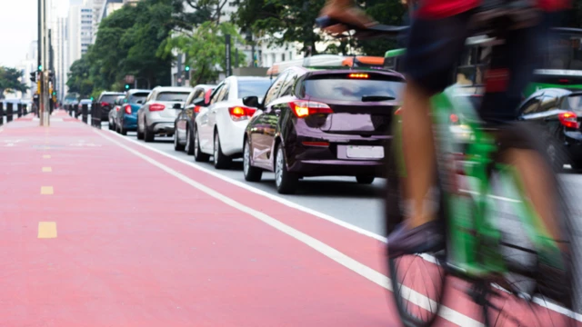 Mujere en bicicleta junto a una calle con tráfico.