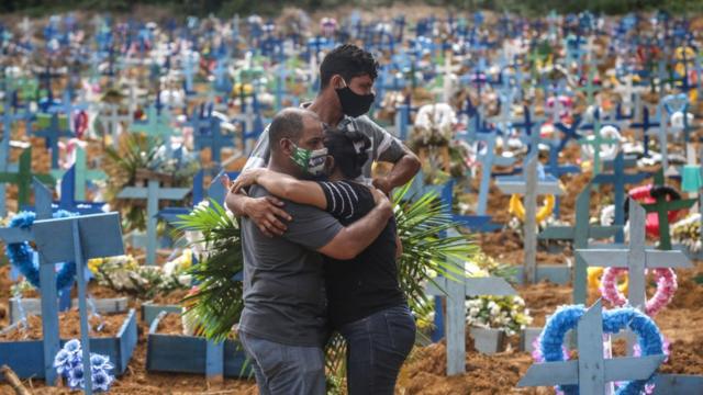 Tres personas abrazándose en un cementerio de Brasil