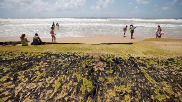 Manchas de óleo e banhistas na beira d'água em praia na Bahia