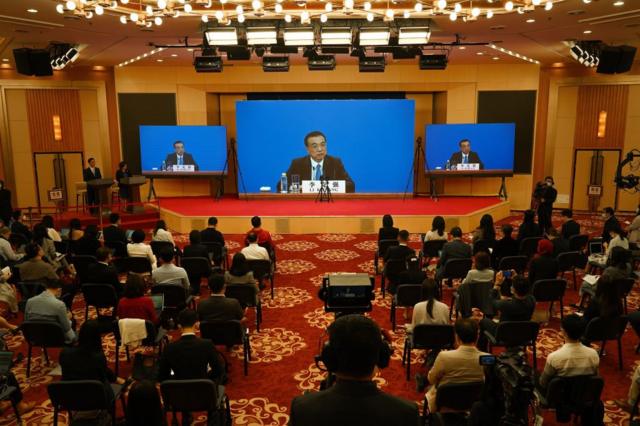 由于疫情，记者会通过视频连线进行。记者们位于北京梅地亚新闻中心，而李克强位于人民大会堂。
