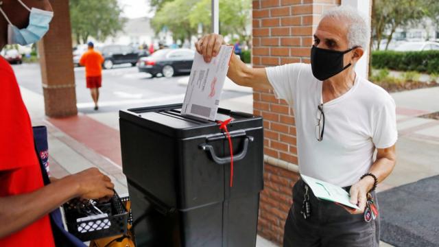 Man in a black face mask returns his mail-in ballot
