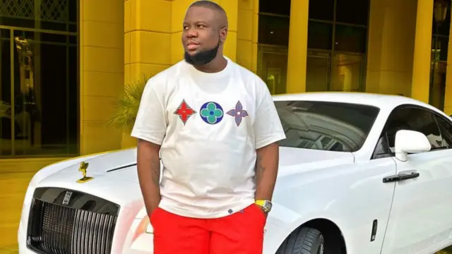 Hushpupi in front of a luxurious car