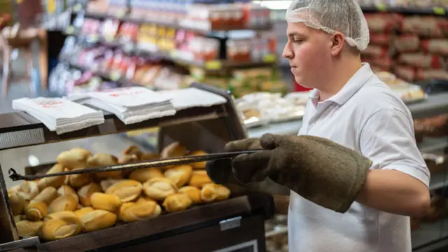 Panadero sacando pancitos de un horno eléctrico en un supermercado