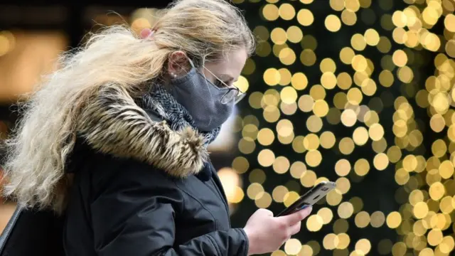 A shopper in a mask walks past Christmas lights in London
