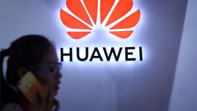 July 8, 2018a woman uses her mobile phone in front of a Huawei logo at Beijing International Consumer Electronics Expo in Beijing.
