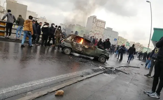 Des manifestants iraniens se rassemblent autour d'une voiture en feu lors d'une manifestation contre l'augmentation du prix de l'essence dans la capitale Téhéran