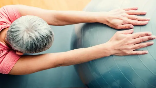 Persona estirándose con una pelota inflable.