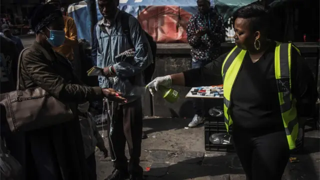 Police spray hand sanitiser on the hands of passers-by on a street in South Africa