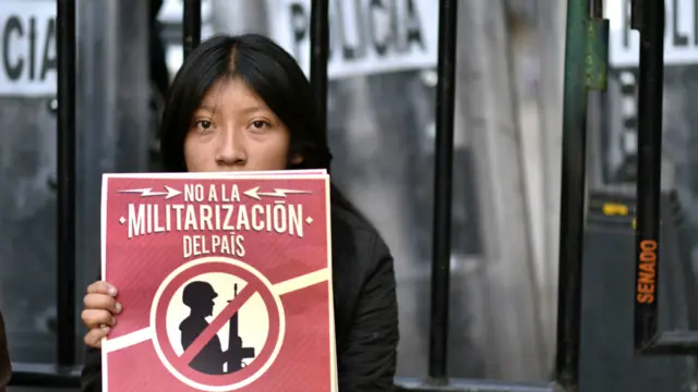Joven con un cartel de protesta contra la militarización del país.