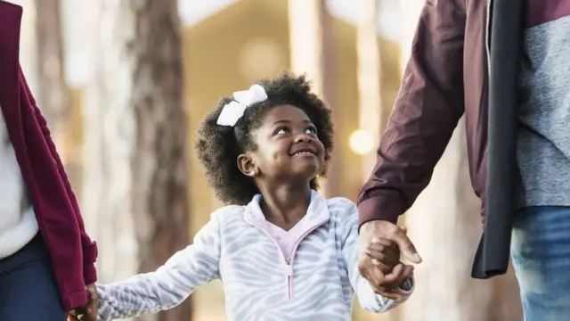 A little girl walking and holding hands with her mum and dad
