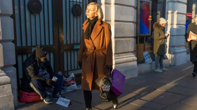 Mujer bien vestida pasando frente a una persona sin hogar.