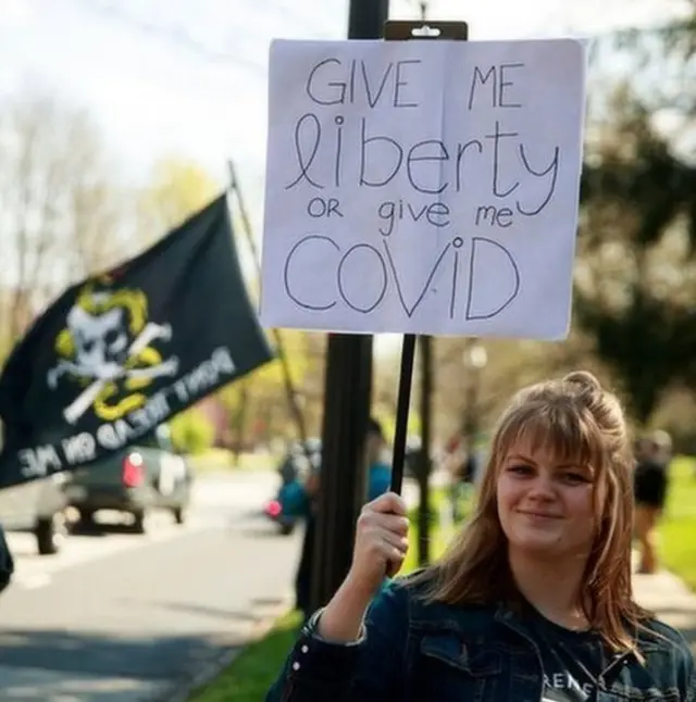 A protester holds a placard: "Give me liberty or give me Covid"