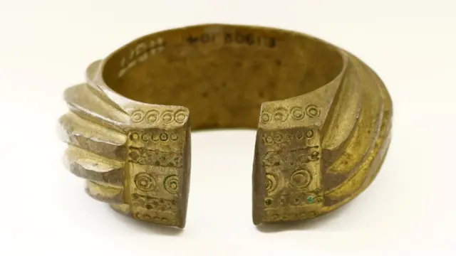 A brass penannular bracelet decorated with heavy slanting bands