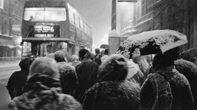 Заснеженные люди ждут автобуса на остановке.