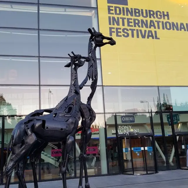 скульптуры жирафов на фоне фестивальной афиши