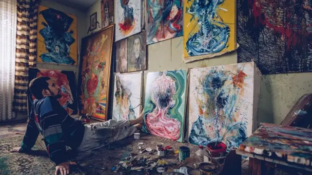 شخص يجلس وحيدا أمام عدد من اللوحات الفنية