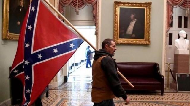 Un simpatizante de Donald Trump entra al Capitolio con una bandera confederada al hombro