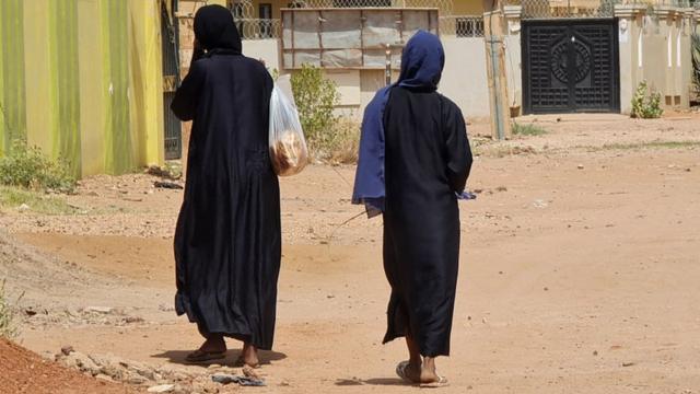 Des femmes portant des sacs à provisions marchent dans une rue vide du quartier de Jabra à Khartoum, le 28 mai 2023.