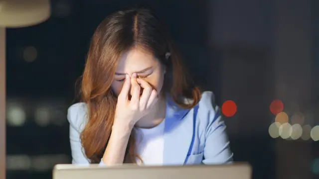 Una mujer con los ojos cansados por la pantalla del computador.