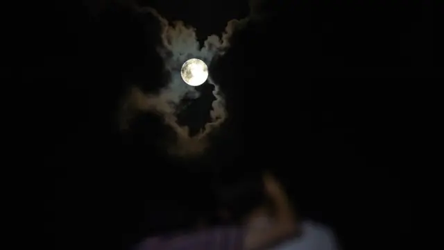 A couple watches as a full moon rises in the background on the Gold Coast on March 31, 2018