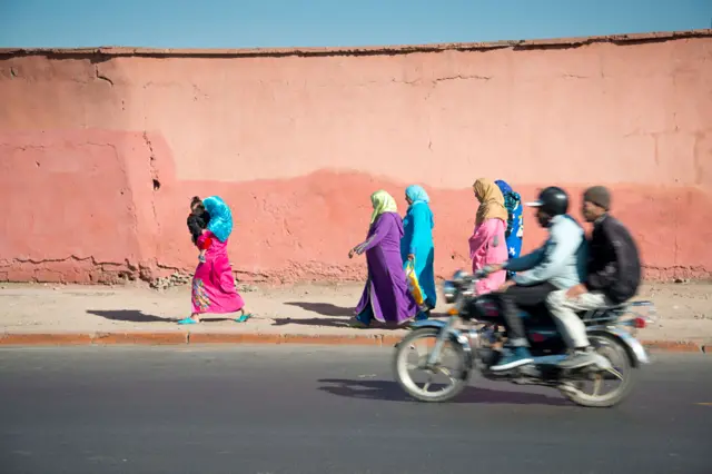 Men on motorbike pass women walking - Marrakech