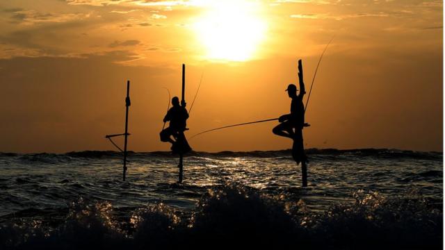 Sombras de homens pescando no meio do mar no Sri Lanka, no que aparenta ser um momento de pôr-do-sol