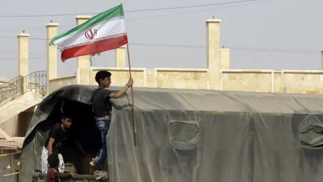 Un adolescente sirio enarbola una bandera de Irán a bordo de un camión que lleva provisiones a Deir Ezzor