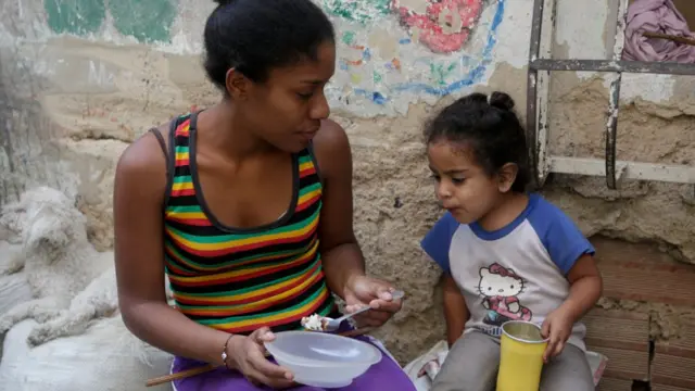 Mãe venezuelana alimentando a filha.