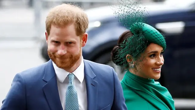 Harry e Meghan sorrindo e caminhando lado-a-lado