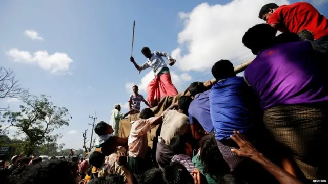 A man uses a cane to control the crowd while providing relief supplies to Rohingya refugees.