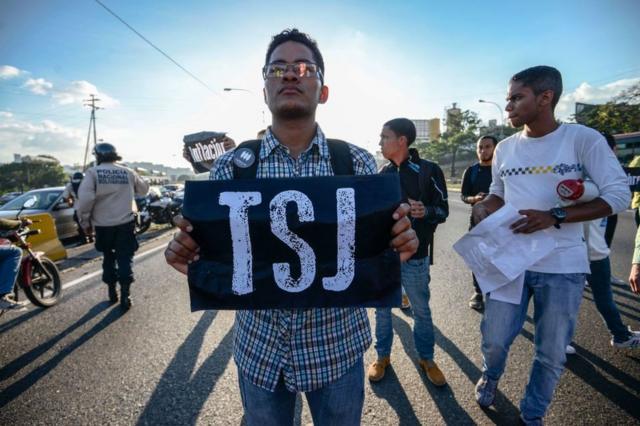 Joven con un cartel que dice "TSJ" protesta en Caracas, Venezuela.
