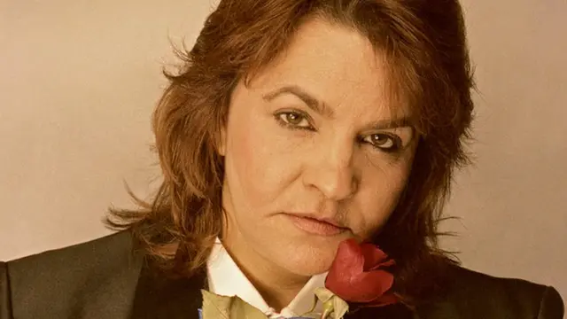 Cassandra Rios posa para foto segurando uma rosa e encarando a câmera