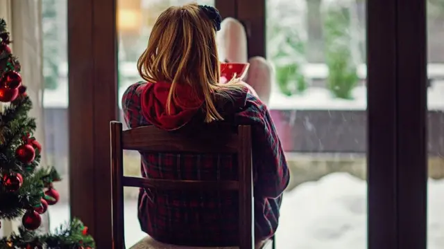 Young woman looking the falling snow outside