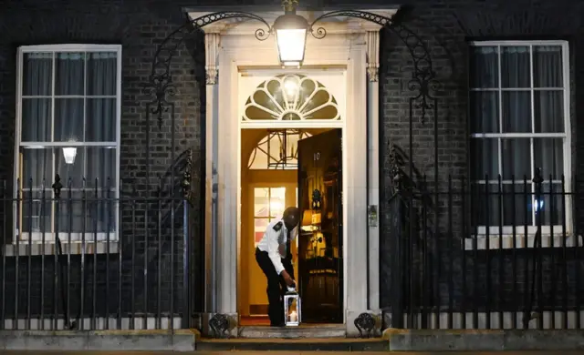 A custodian places a lit candle outside 10 Downing Street to mark one year of Covid-19 and to honour those who lost their lives to Covid-19 in London, 23 March 2021.