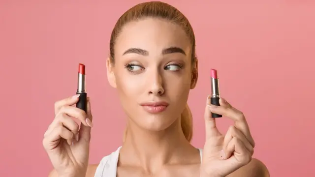 Una mujer con mirada indecisa sostiene un pintalabios en cada mano.