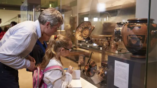 Profesores y alumnos observando artefactos históricos en exhibición en un museo.