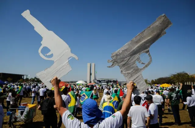 Manifestante segura cartazes em formato de armas, durante protesto pró-Bolsonaro em Brasília em julho