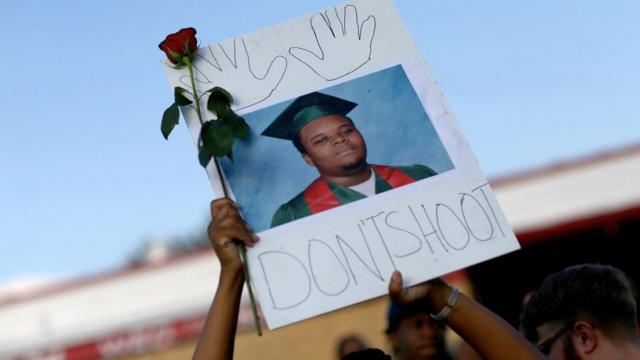 一位游行示威者举着迈克尔·布朗（Michael Brown）的照片，照片上的这个18岁男孩于2014年在美国密苏里州弗格森（Ferguson, Missouri）在未携带武器的情况下遭一名警察开枪杀死。