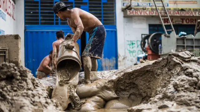 Hombre botando lodo de su propiedad con ayuda de un balde.