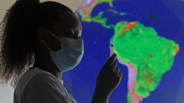 Enfermeira com máscara segurando seringa, com mapa do Brasil atrás
