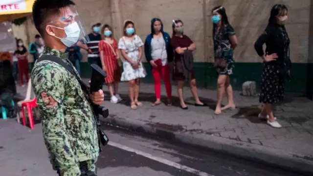 A policeman stands guard as Catholic faithful queue to attend the first of nine dawn masses amid the pandemic outside the gate of a church in Manila on December 16, 2020