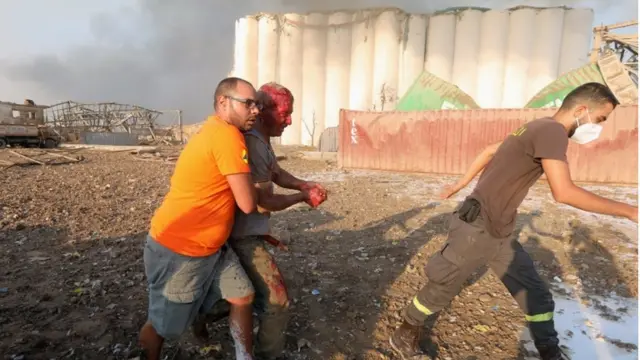 Dos hombres ayudan a otro herido a caminar tras la explosión en Beirut.