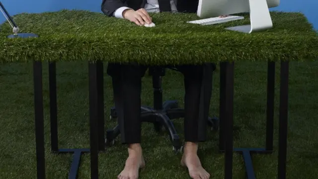 Hombre con pies descalzo en une escritorio con hierba artificial.