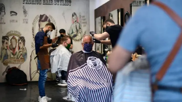 Diversos barbeiros atendem clientes, distantes uns dos outros e usando máscaras,site da betbarbearia na Alemanha