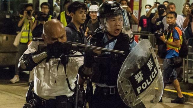 香港新界葵涌警署外一名警署警长（左）举起雷鸣登霰弹枪指向示威者（30/7/2019）
