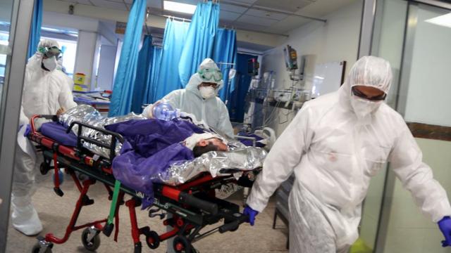德黑兰某医院身穿全身保护服的救护员把一名病人推进医院大厅（2/3/2020）