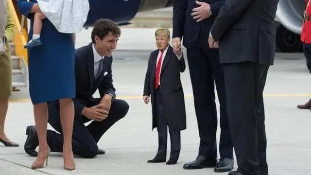 ডোনাল্ড ট্রাম্প একজনের হাত ধরে আছেন দাঁড়িয়ে আছেন এবং তাঁর সামনে হাঁটু গেড়ে বসে হাসছেন কানাডার প্রধানমন্ত্রী জাস্টিন ট্রুডো।