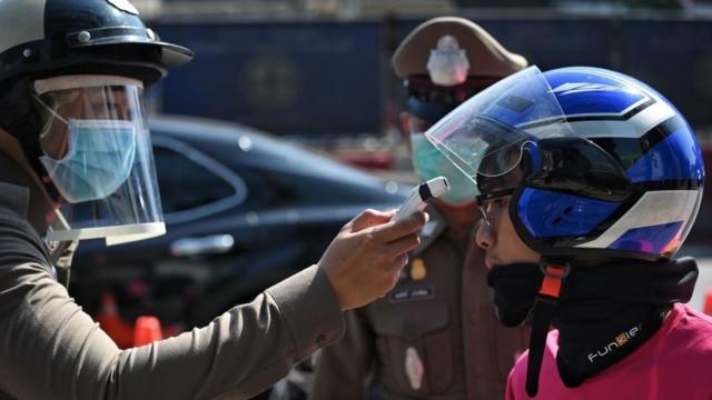 Một thành viên Cảnh sát Hoàng gia Thái Lan đo nhiệt độ của một người lái xe giao thức ăn trong biện pháp phòng ngừa chống lại sự lây lan của virus corona tại một trạm kiểm soát ở ngoại ô Bangkok