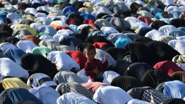 A small child stands amid a crowd of Muslims knelt in prayer during Eid al-Adha in Manila